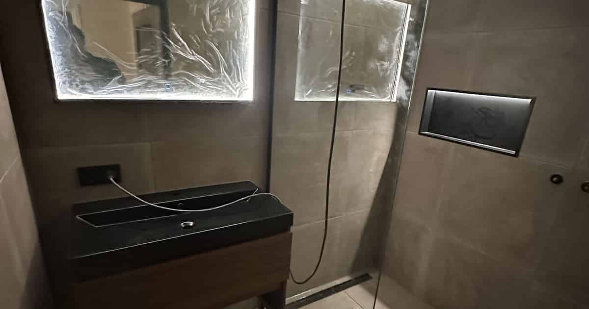 Afgewerkte badkamer met inloopdouche en verlichte spiegel bij familie Vellema in Drachten